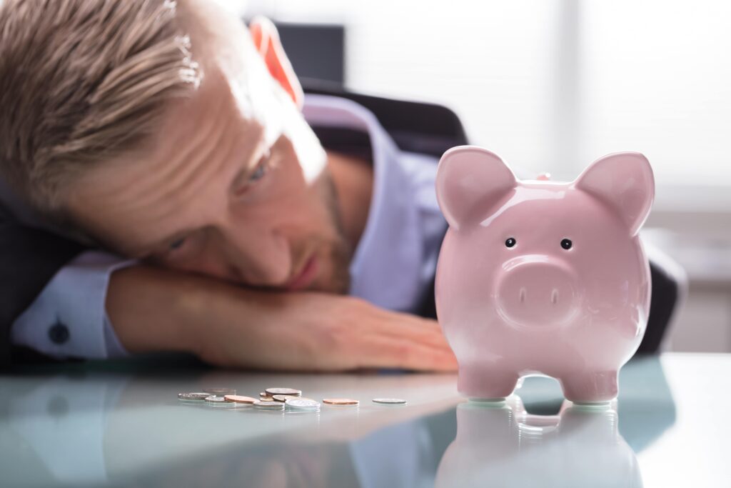 A man looking defeated in front of a piggy bank to imply the weight of federal tax liens and to contact a tax lien attorney.